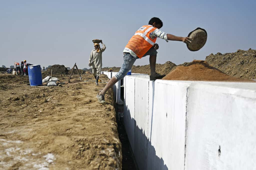 A worker carries sand in a container on his head at an under construction sewerage system near the village of Dholera, Gujarat, India, on November 22, 2017. (Photographer: Anindito Mukherjee/Bloomberg)